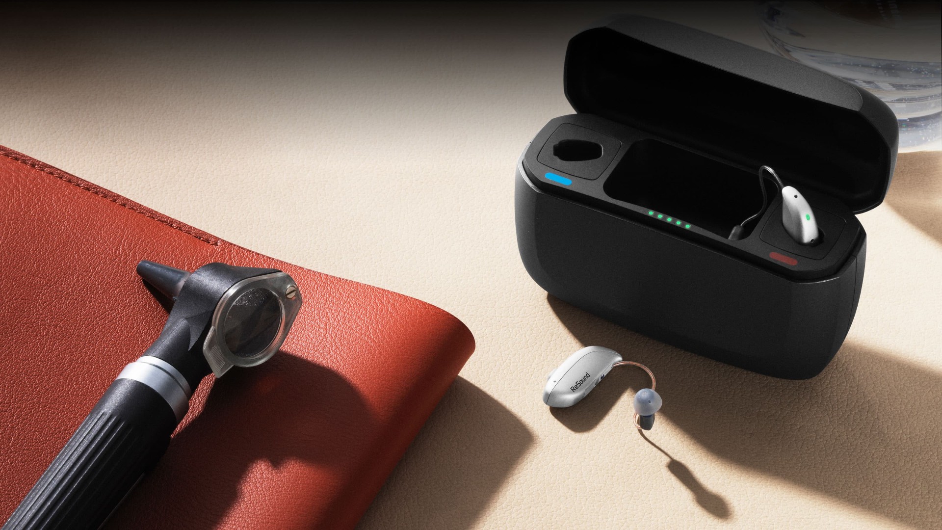 A small rechargeable behind-the-ear hearing aid held between an audiologist's fingers