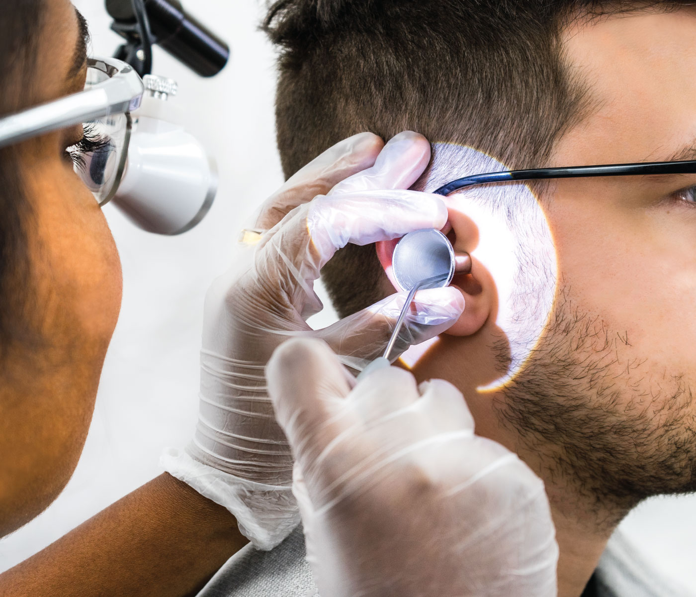 An audiologist removing ear wax with a microsuction handpiece while viewing the ear through magnifying loupes