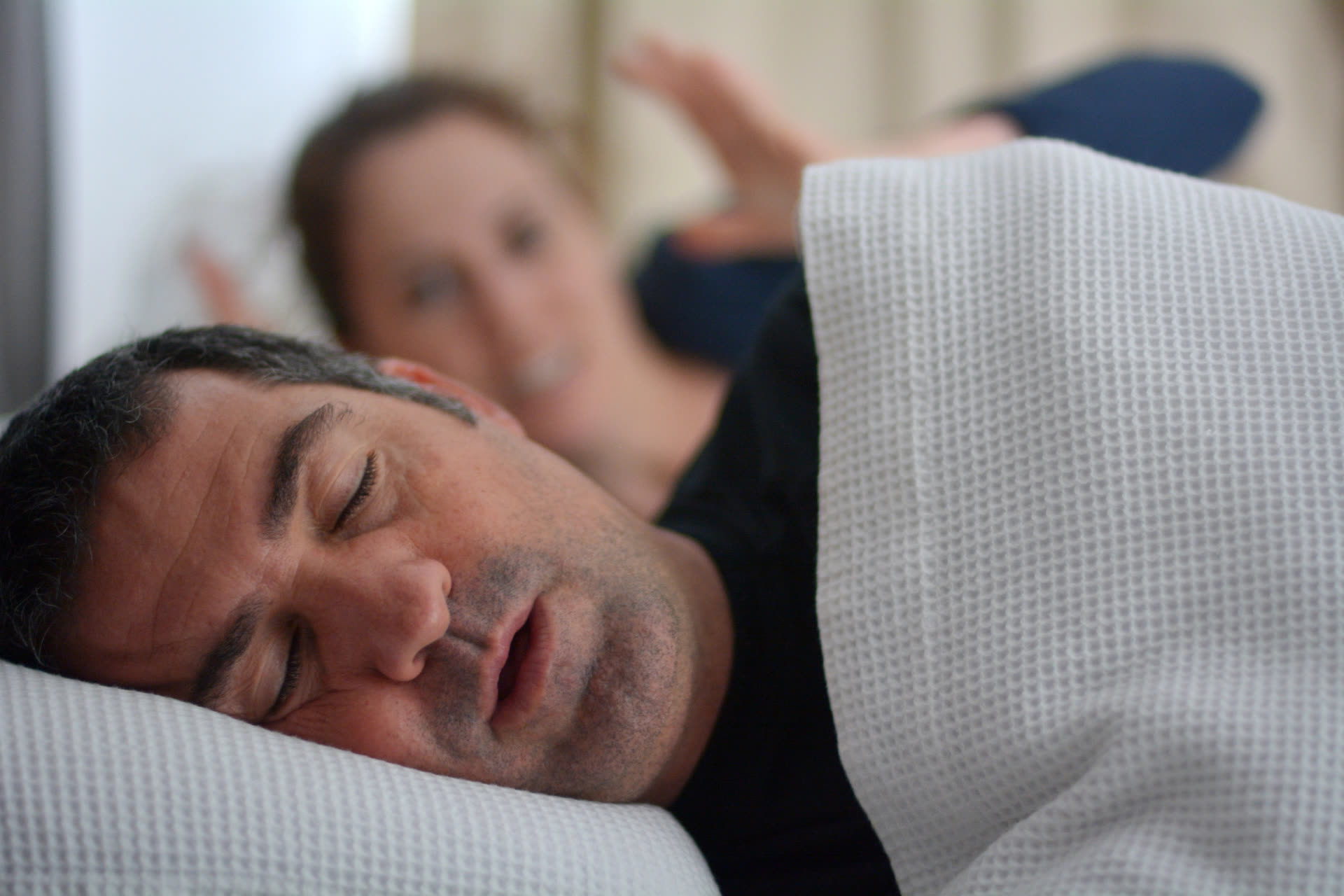 A couple lying awake in bed at night, one kept awake by the other's snoring