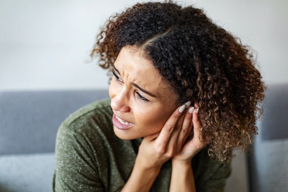 A woman holding the side of her head, wincing with the pressure of a blocked ear canal