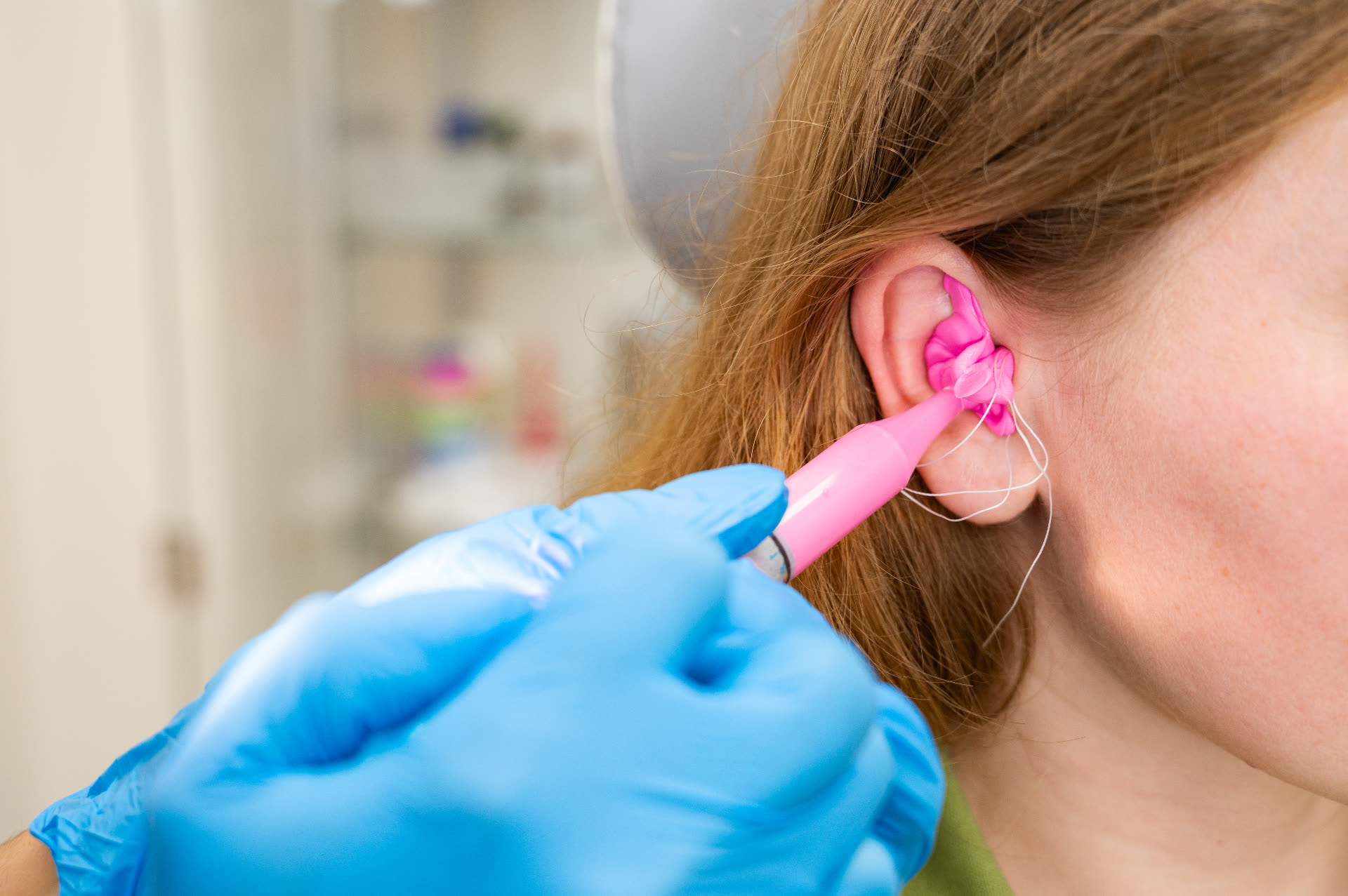 An audiologist taking an ear impression with bright pink moulding material